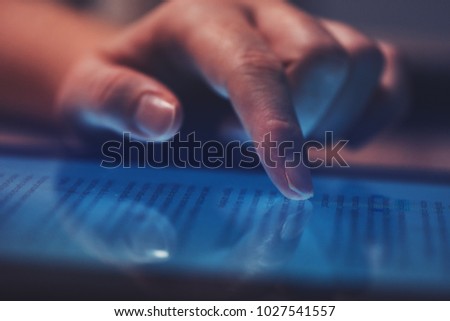 Extreme close up of female finger using digital tablet computer at home in the evening to read the news online, selective focus Royalty-Free Stock Photo #1027541557