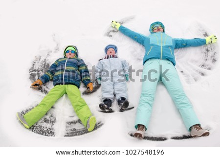 A young lady in a blue ski suit plays football with children in the snow. Yellow sled, sunglasses, bright clothes. Girl happy outdoors. Fun winter vacation for the whole family. Green soccer ball