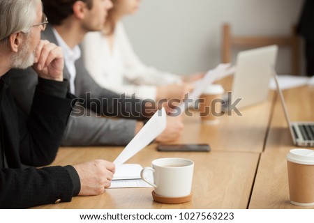 Attentive senior businessman holding documents focused on listening at group meeting, aged experienced investor, client or company executive participating training conference business seminar concept Royalty-Free Stock Photo #1027563223