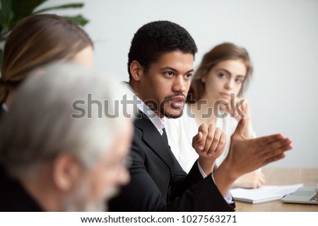 Serious african american ceo giving instructions at diverse team meeting, confident black leader talking delegating work, serious dark-skinned executive manager speaking appealing to colleagues group Royalty-Free Stock Photo #1027563271
