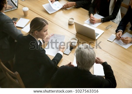 Negotiations concept, different businesspeople discussing deal details at group meeting, young and senior partners team thinking talking consulting about contract sitting at conference office table Royalty-Free Stock Photo #1027563316