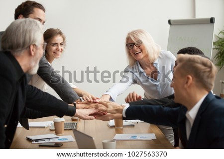 Happy smiling corporate team of senior executives and young employees join hands together at group meeting, business people celebrating success achievement unity, promising help support in teamwork Royalty-Free Stock Photo #1027563370