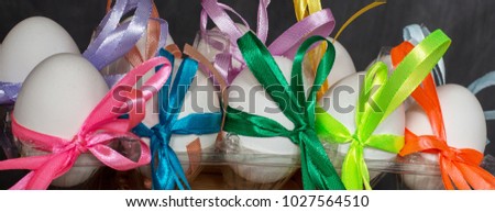 White Easter eggs are decorated with colorful ribbons. Eggs lie on a dark ground