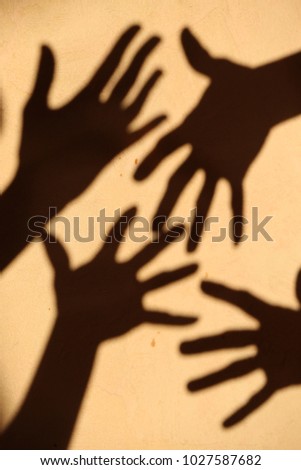 Close up interior view of four human hands shadows projected on a beige wall by the sunlights. Dark silhouettes of the twenty fingers. Isolated elements on the surface wall. Absract graphic  image.