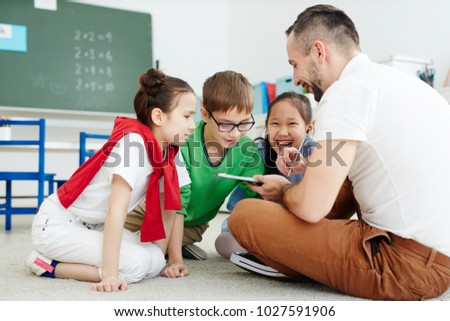 Contemporary teacher drawing something funny and showing the picture to his elementary learners