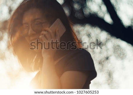 attractive cute asian young girl talking with smart phone. sunset moment. light and flare effect. filtered image to vintage tone. cute asian woman short hair with blurred background. hipster style