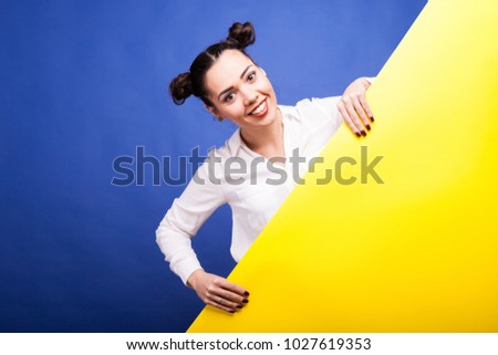 Happy smiling woman holds a yellow poster in hands with copy space available over blue background in studio photo