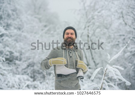 Man in thermal jacket, beard warm in winter. Winter sport and rest, Christmas. skincare and beard care in winter. Bearded man with skates in snowy forest. Temperature, freezing, cold snap, snowfall.