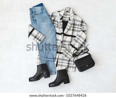 Blue jeans, striped coat, small black cross body bag and leather ankle boots on grey background. Overhead view of woman's casual day outfits. Trendy hipster look. Flat lay. Royalty-Free Stock Photo #1027648426