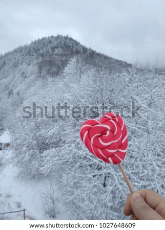 Sweet romantic picture with candy heart in the hand on snowy mountains background