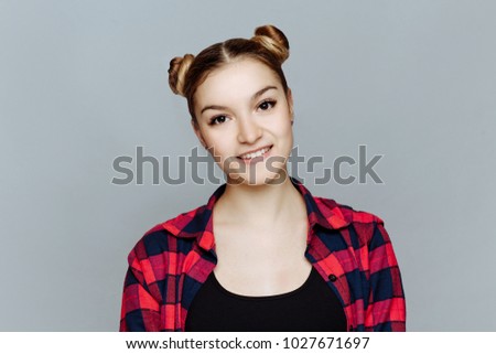 Body language and emotion. Portrait close up on a white background in studio. The young girl the blonde in a plaid shirt and a black undershirt looks in the camera and friendly smiles.