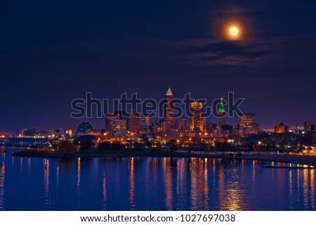 A bright super moon rises high above the city of Cleveland Ohio and Lake Erie waters at dusk