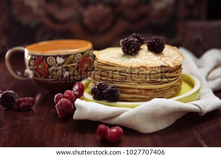pancakes with frozen berries pile in a green plate with a cup of milk on a dark wooden table 