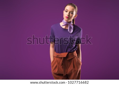 serious girl with hands in pockets looking at camera isolated on purple Royalty-Free Stock Photo #1027716682