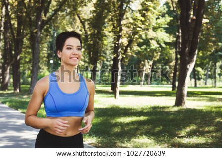 Young sporty woman running in green park during morning workout, copy space