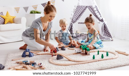 family mother and children play a toy railway in the playroom
