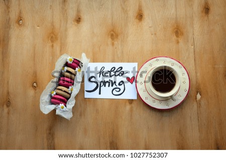 A note with hello Spring text and colorful macaroons with a cup of coffee on rustic wooden table 