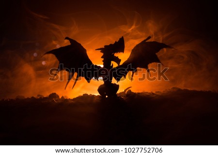 Silhouette of fire breathing dragon with big wings on a dark orange background. Selective focus
