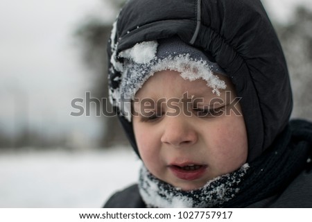 The sad face of a little boy in the snow in winter.