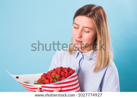 Close up of young woman holding bouquet of strawberries on blue background.