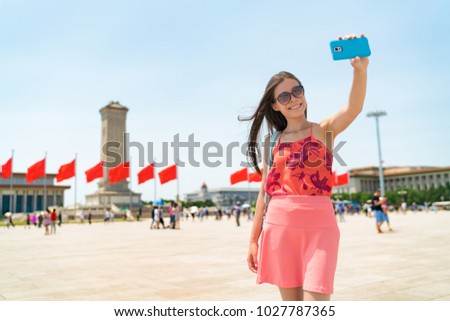 Asian tourist woman taking selfie photo with phone in Beijing, China. Asia travel famous destination girl holding cellphone visiting Tiananmen Square, popular tourism attraction. Summer vacation.