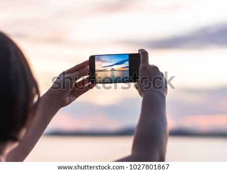 Smartphone camera in tourist woman person’??s hands who taking photo on touch screen of beautiful seascape sky with clouds during sunset at golden happy hour at dawn