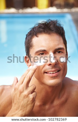 Attractive man applying sunscreen to his face with his finger