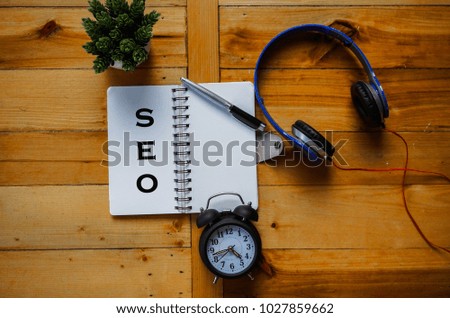 SEO written on note book with pen, headphone and clock.