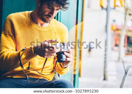 Cropped view of male amateur dressed in yellow sweater making setting on display of vintage camera for cool pictures.Professional photographer checking photos on antique device resting in coffee shop