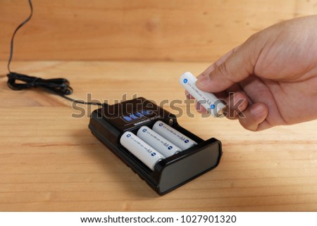 Hand holding battery size AA rechargeable with Charger Plug in power outlet adapter on wooden table Royalty-Free Stock Photo #1027901320