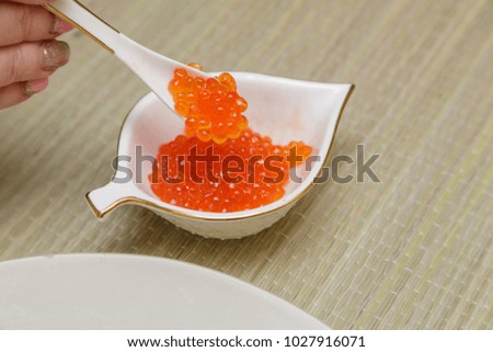 A woman takes a spoonful of red caviar from a cup, a horizontal frame