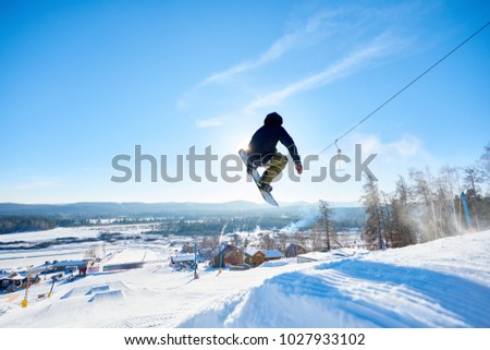 Back view action shot of young man performing snowboarding stunt jumping high in  sunlight at ski resort, copy space