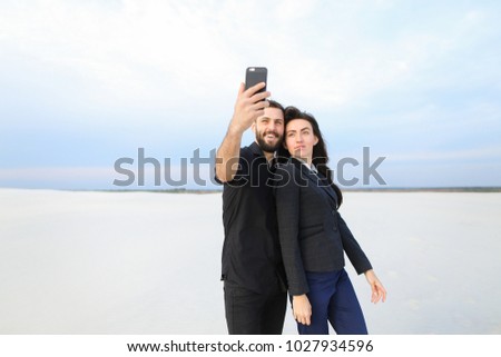 couple test camera in new smartphone, boyfriend and girlfriend taking selfies. Fellow in black shirt and girl in suit posing for photo. Concept of innovative technologies, using gadgets to m