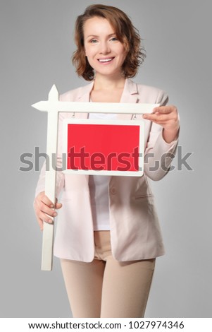 Real estate agent with blank sign on grey background