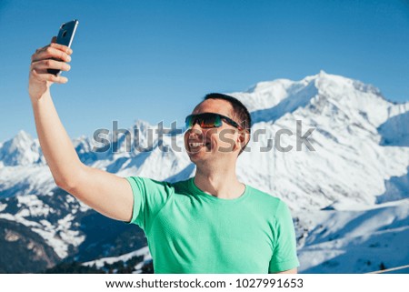 Handsome young male taking a picture with his smartphone. Mont Blanc in the background.