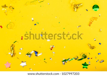 Bright colorful carnival or party scene of metalic colorful confetti on yellow background. Flat lay style, birthday or party greeting card background