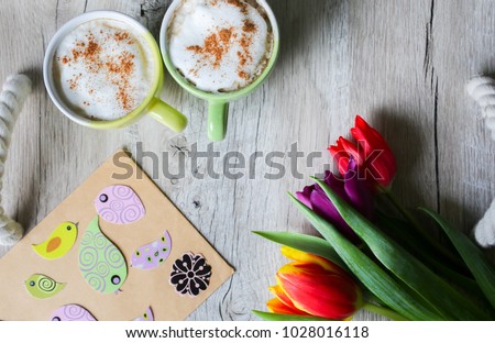 Tulips on wooden with two cups of coffee. Invitation postcard for mother's day or international women's day. Spring paper birds on craft paper envelope. Handmade origami. Punchy pastels.Easter picture