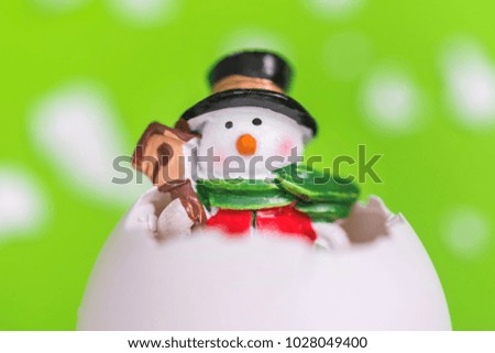 Small Christmas toy snowman in the white eggshell on a green background