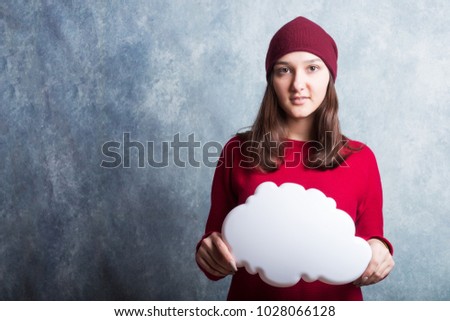A young pretty smiling girl in a red sweater against the background of a modern gray loft-style wall holds white clouds in her hands. She looks at the viewer. Copy space.