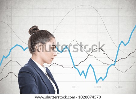 Side view of a calm and beautiful young european woman with a bun wearing a white sweater. A concrete wall background with graphs on it