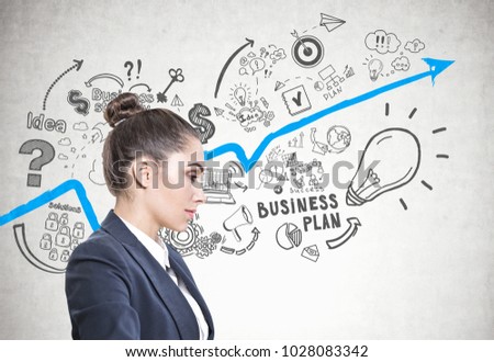 Side view of a calm and beautiful young european woman with a bun wearing a white sweater. A concrete wall background with a business plan sketch