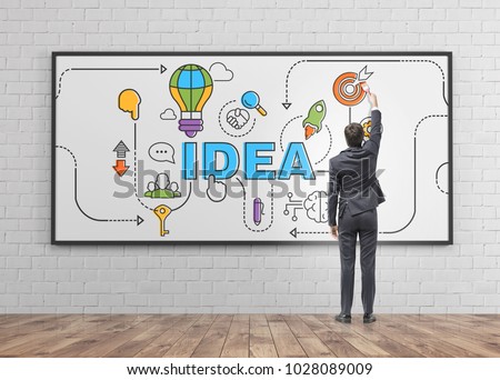 Rear view of a businessman drawing a colorful idea sketch on a whiteboard in a wooden floor room. Concept of creativity in business
