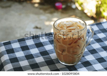 Iced milky tea on black and white tablecloth with blurred nature background