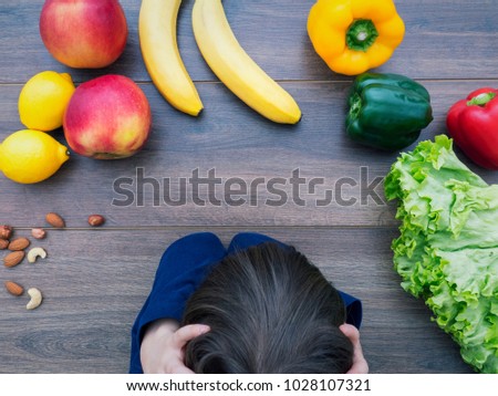 Angry kid sitting at the table looking at healthy vegetables and fruit