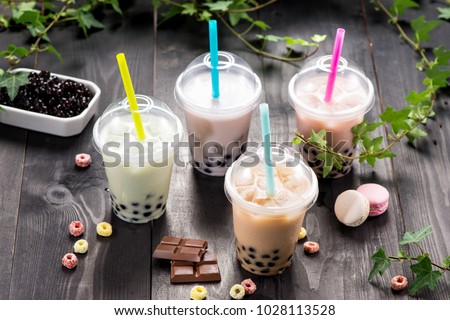 Variety of bubble tea in plastic cups with straws on a wooden table.