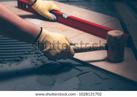 The working tiler knocks on the tile with a Tile Mallet, the professional checks the building level