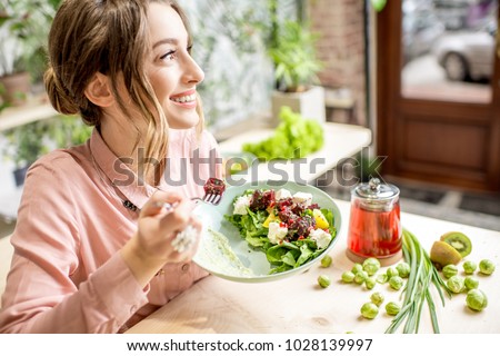 Young woman eating healthy food sitting in the beautiful interior with green flowers on the background Royalty-Free Stock Photo #1028139997