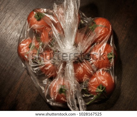 tomatoes in transparent plastic bag on brown wooden surface, above, dark tones - close up