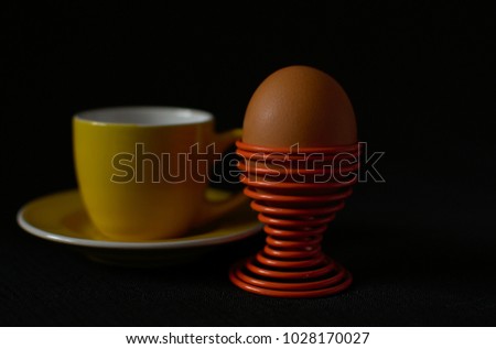 Orange hard boiled egg on the spiral orange egg stand infront of the coffee cup in the black blackground 