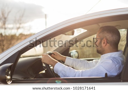 handsome young man at sunset inside the car looking on the mirror. Travel and lifestyle. Outdoors